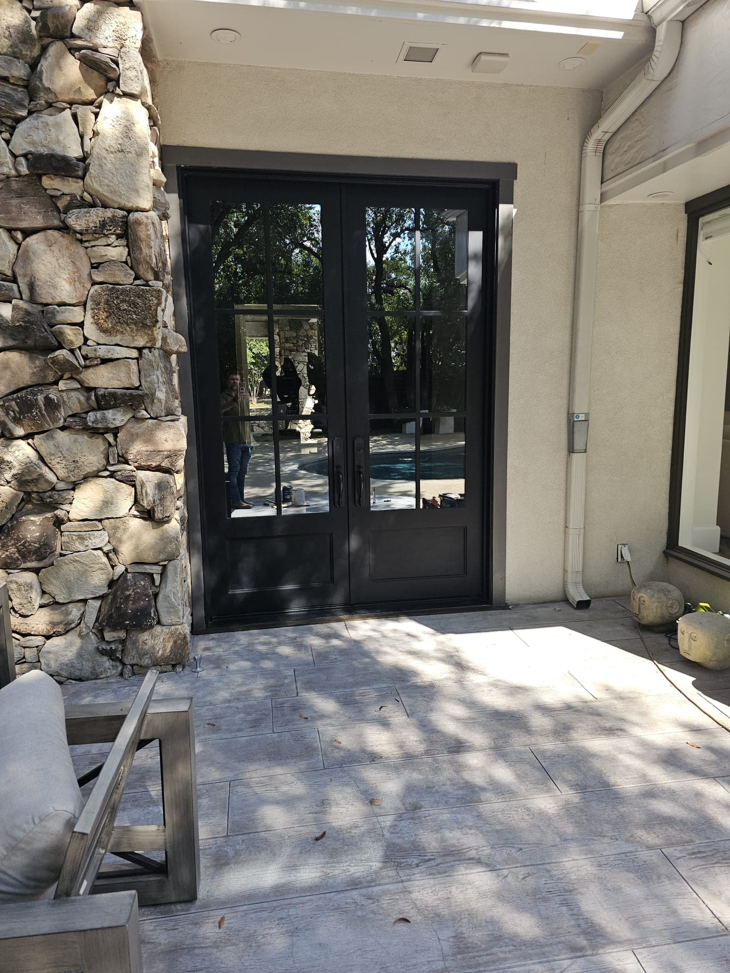 Black-framed French double doors with divided lights, set into a stone and stucco wall opening onto a stamped concrete patio