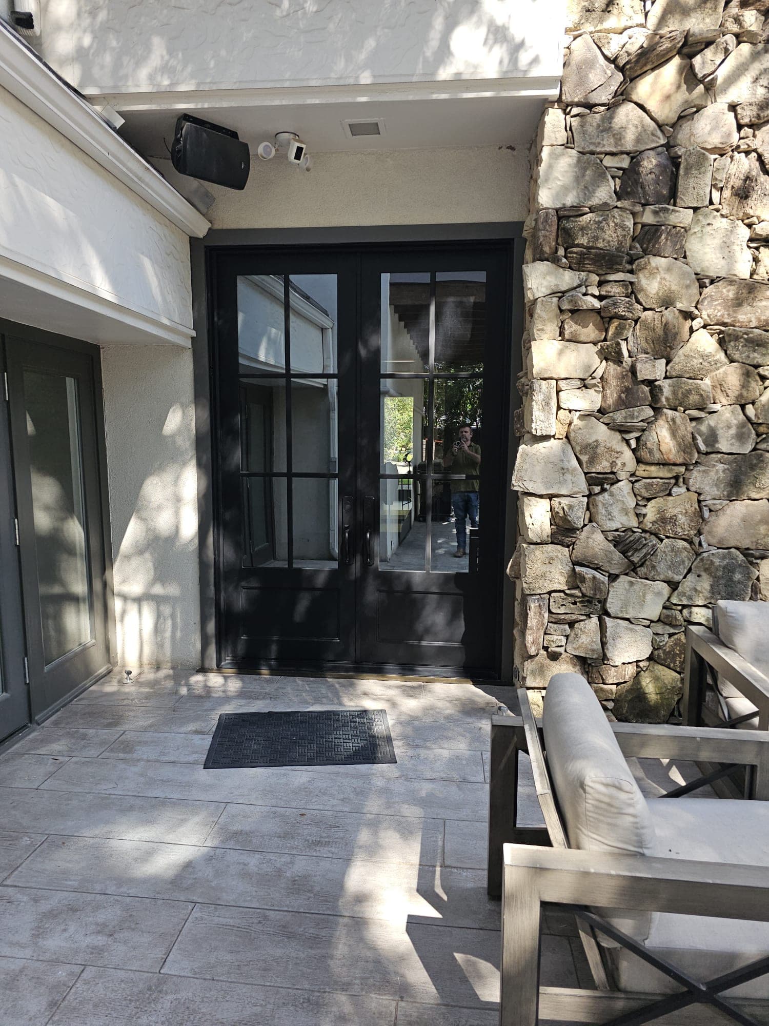 Black French doors with divided lights beside a stone column on a covered patio