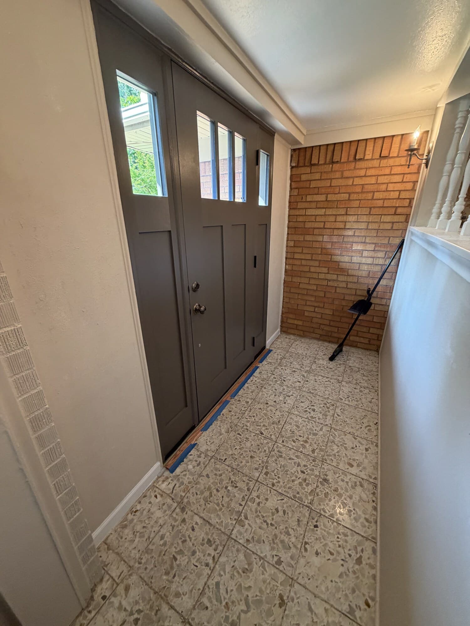 Interior angle of the front door and sidelight against a brick wall, terrazzo floor with painter's tape still at the threshold