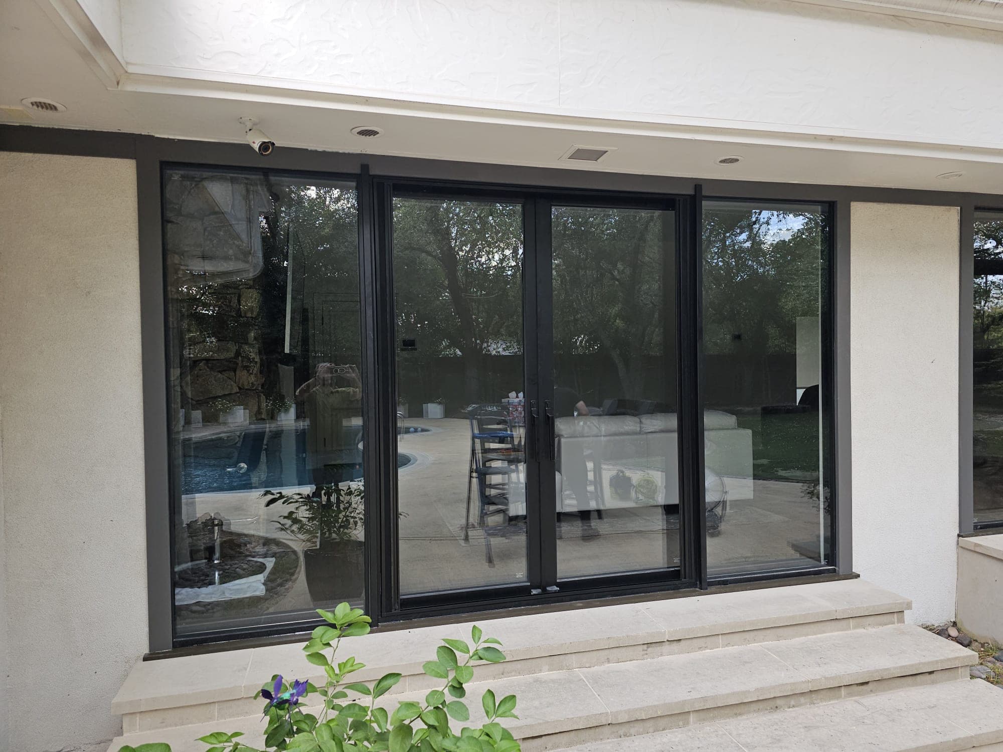 Black-framed multi-slide door system wrapping a corner of the house above a set of stone steps