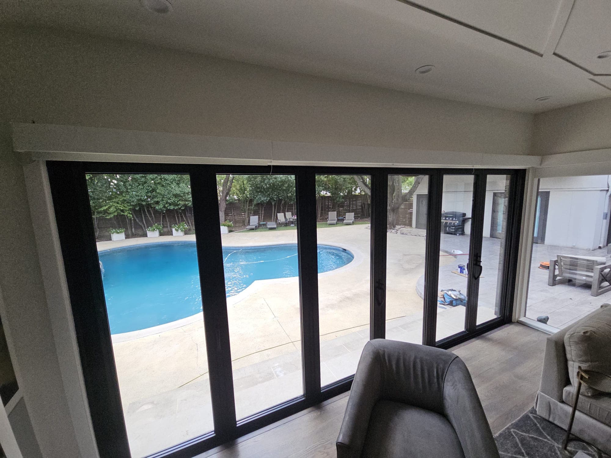 View from inside through an opened multi-slide door system to a swimming pool and patio furniture