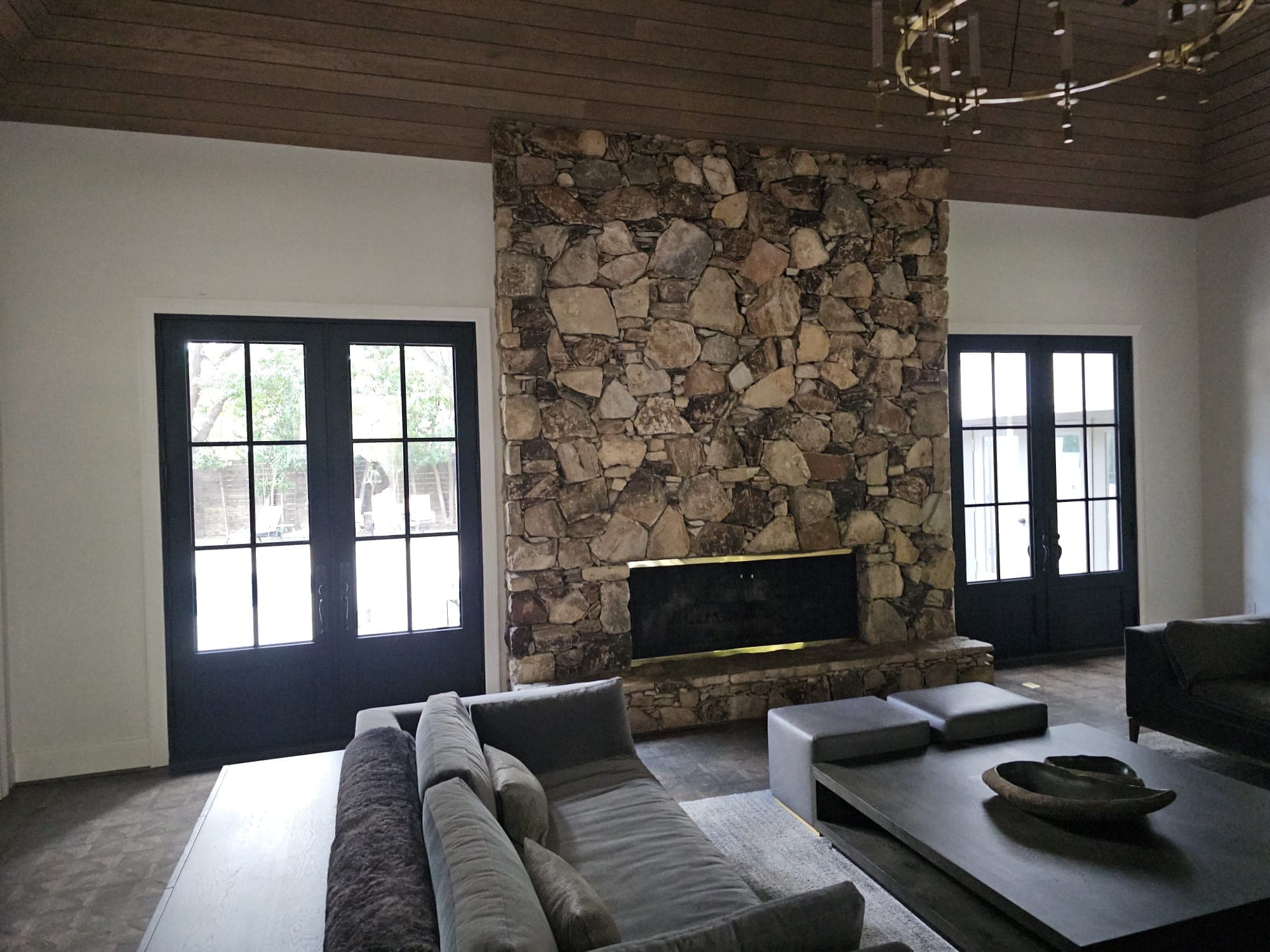 Interior living room with a floor-to-ceiling stone fireplace flanked by two sets of black French doors