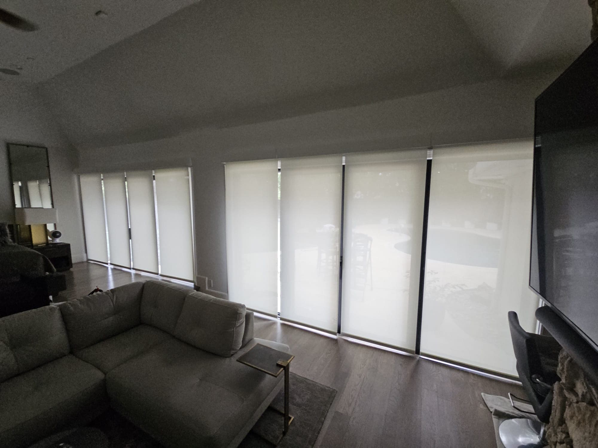 Interior living room with roller shades drawn across a full glass wall behind a sectional sofa