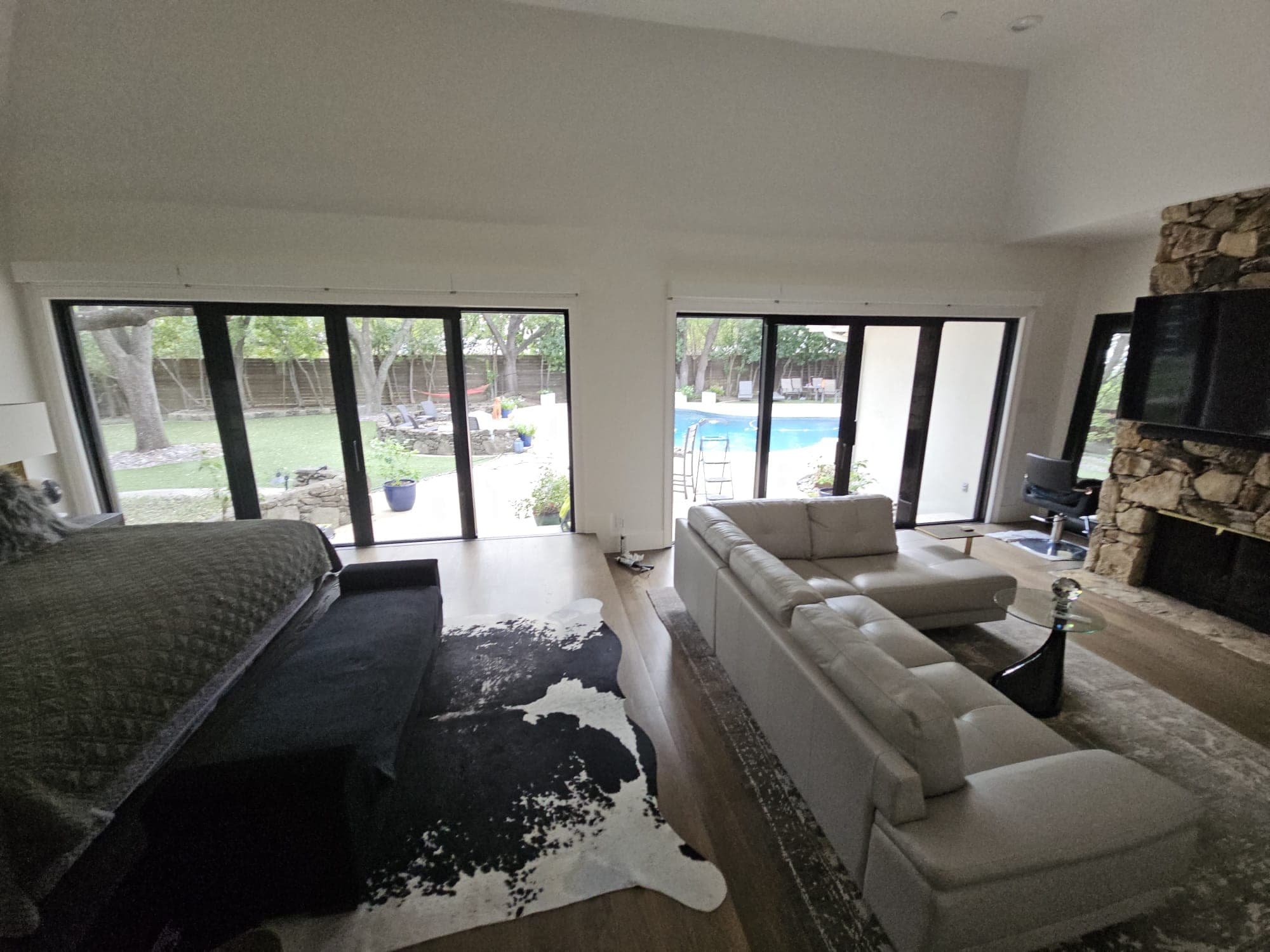 Interior room with black-framed sliding doors along two walls looking out to a pool deck and mature trees