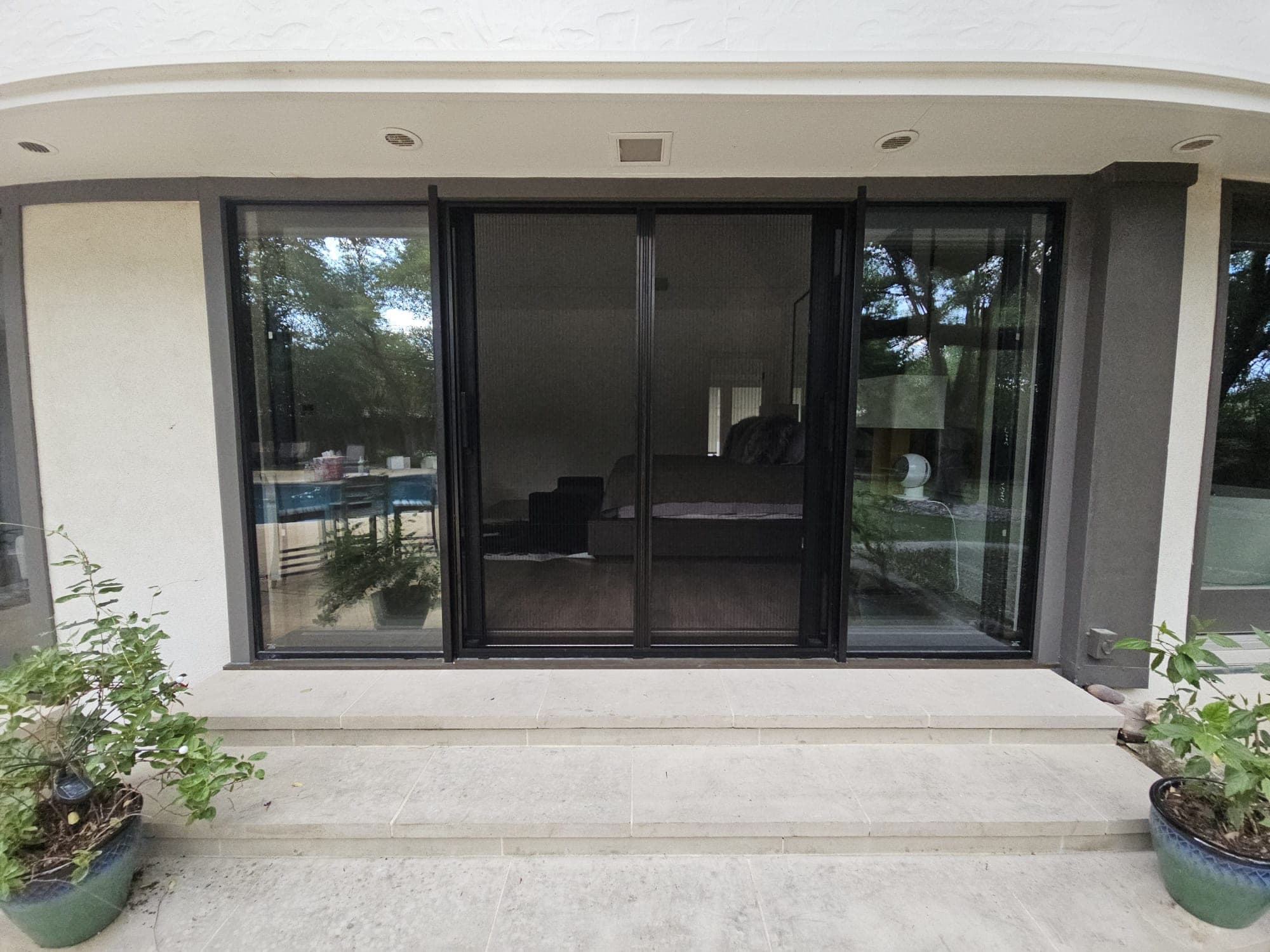 Black-framed sliding door system with an integrated screen panel, flanked by potted plants on a stone step