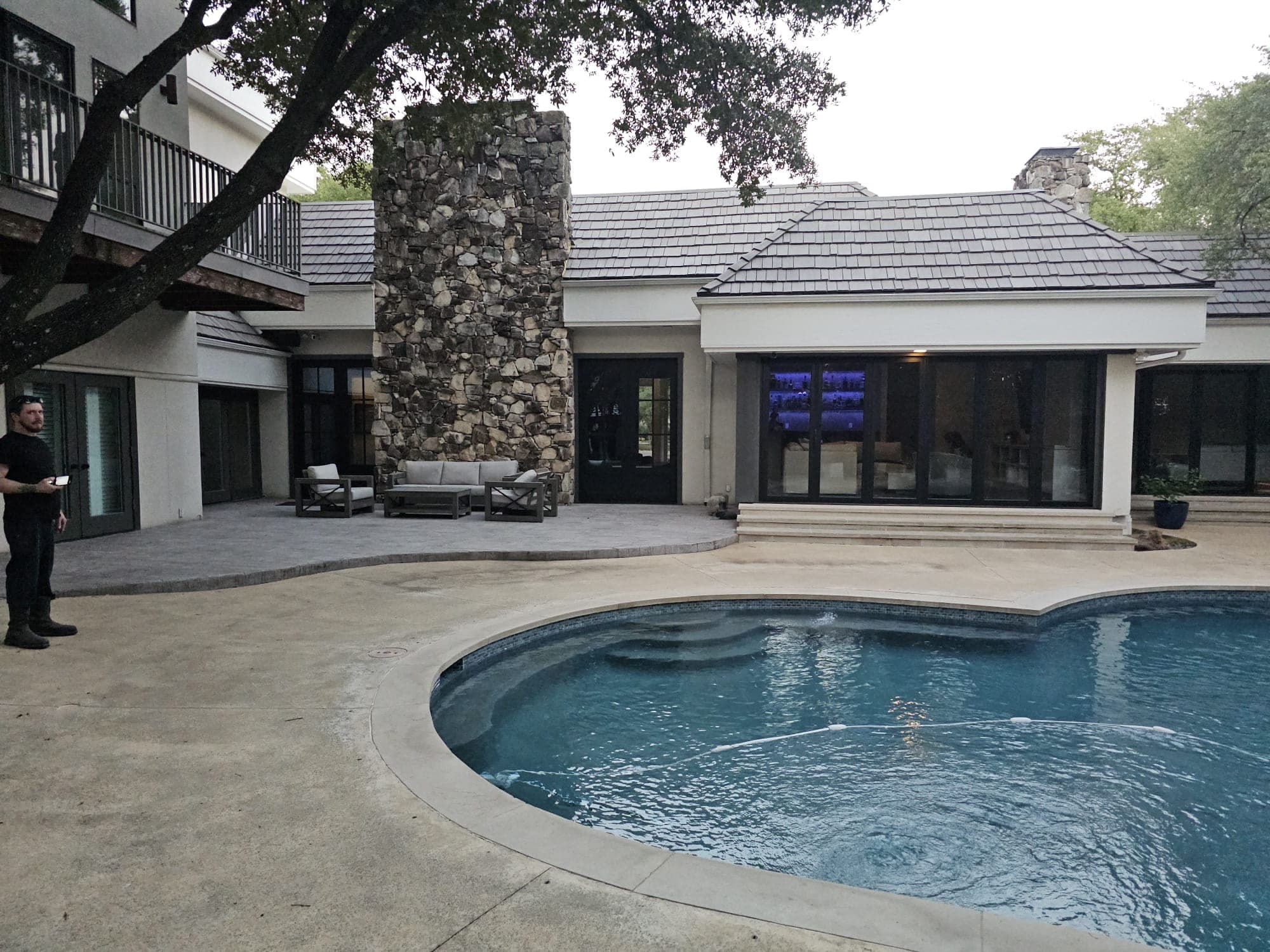 Rear elevation of a house across the pool with a member of the crew on the deck during the install