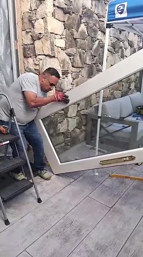 An installer carrying a glazed door panel toward the opening beside a stone wall