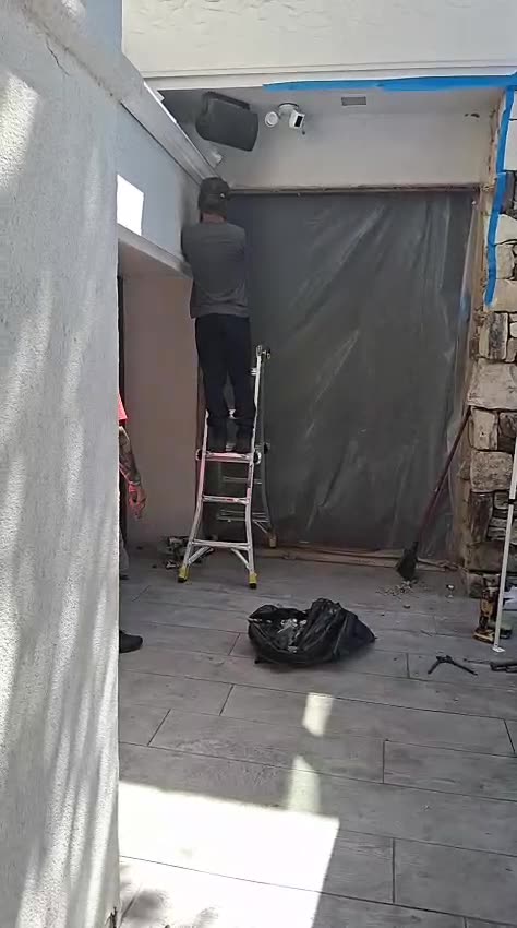 An opening masked with plastic sheeting while an installer works from a ladder
